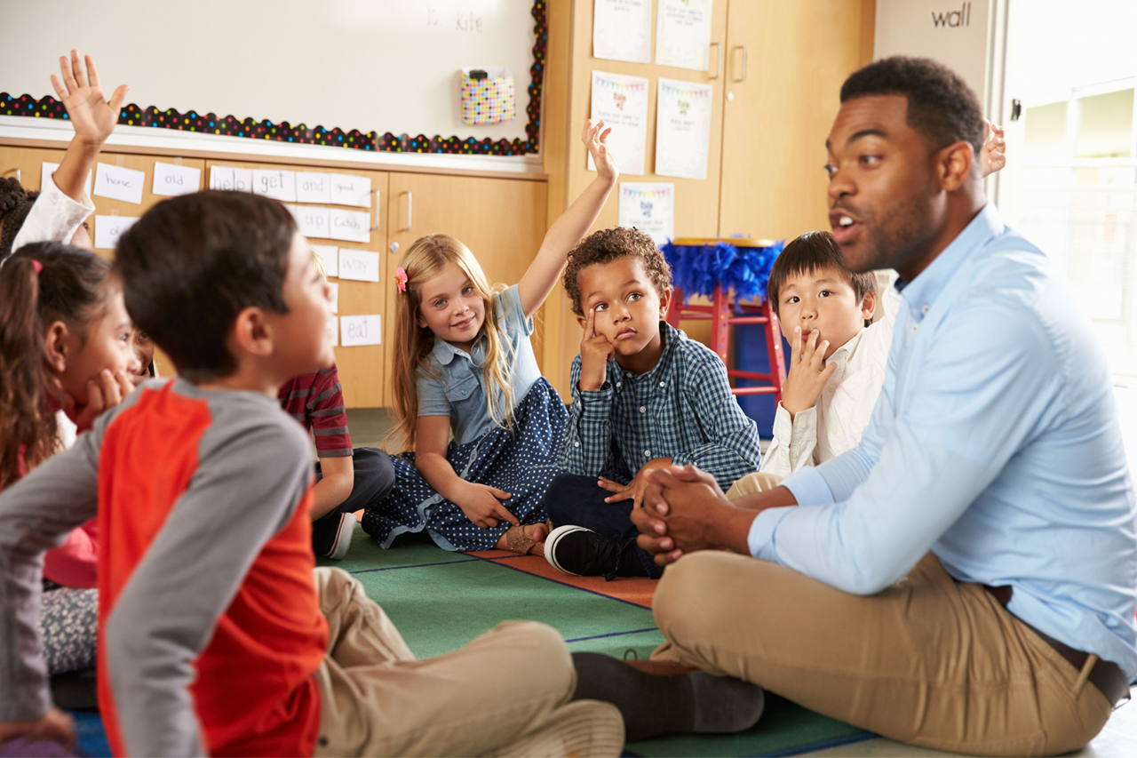 Teacher sitting on floor teaching diverse group of young students
