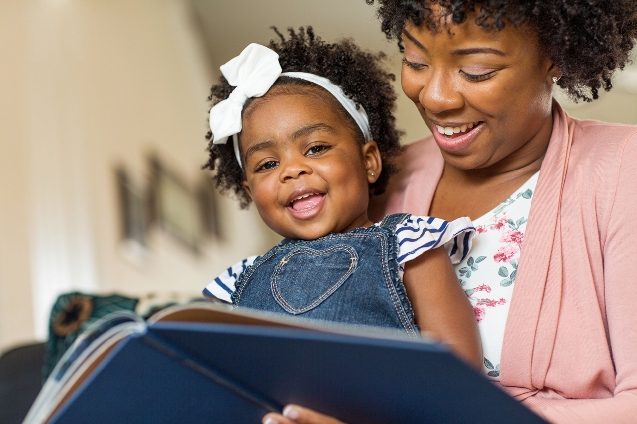 Toddler smiling while reading with adult