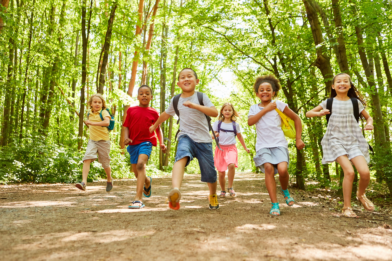 Group of elementary aged kids running through woods on trail